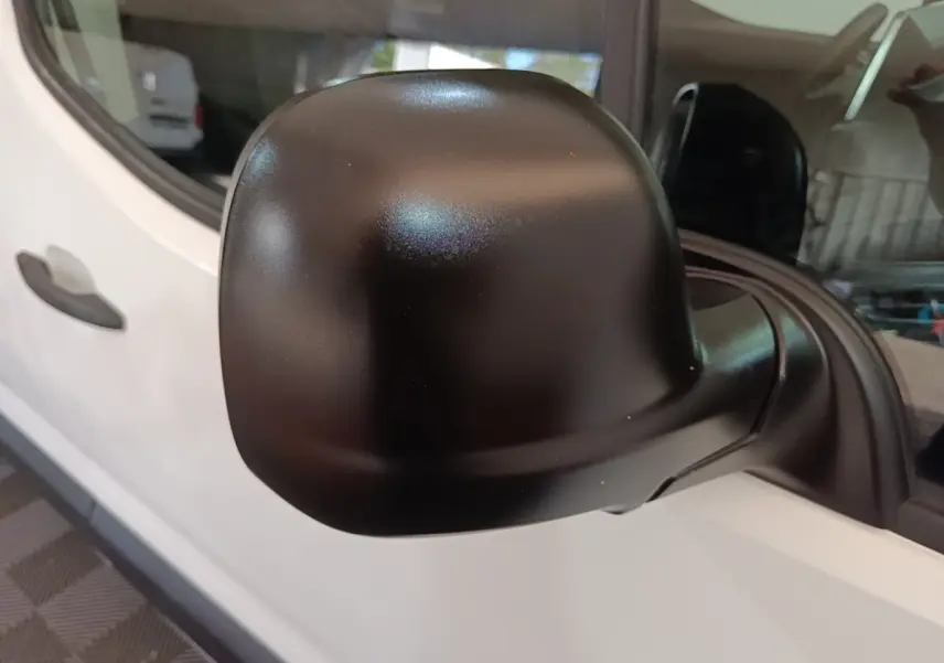 Rétroviseur noir en gros plan sur le côté gauche d’un Peugeot Partner blanc, vue rapprochée de la porte avant.