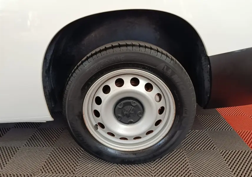 Gros plan sur la roue avant droite en jante acier du Peugeot Partner blanc, avec partie de la carrosserie visible.