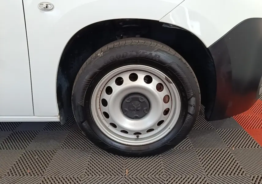 Gros plan sur la roue avant gauche d’un Peugeot Partner blanc avec jante acier et pneu Goodyear.