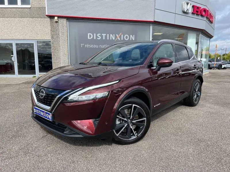 Vue 3/4 avant d'un Nissan Qashqai e-POWER 2023 Rouge Passion avec jantes alliage 19 pouces devant un concessionnaire.
