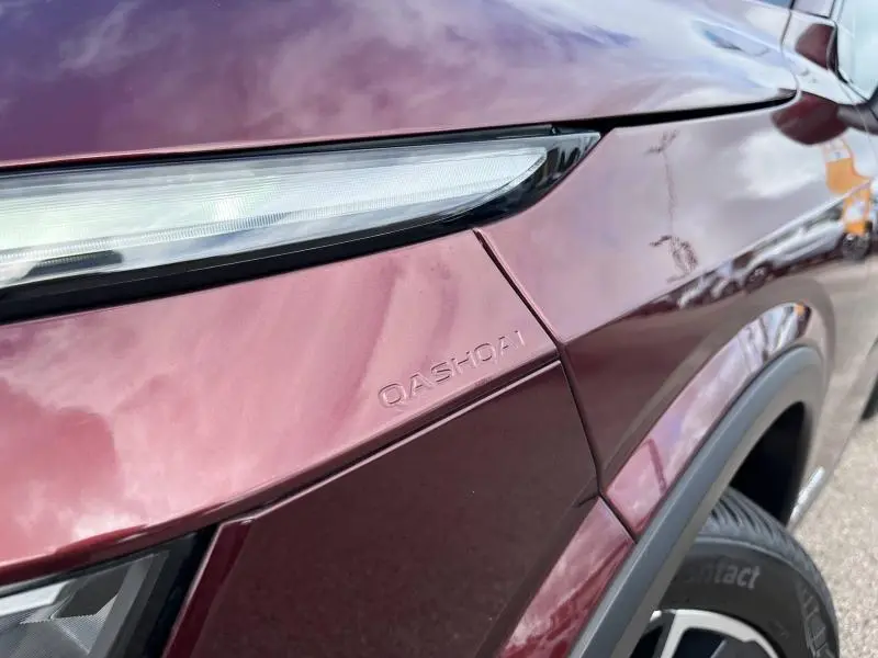 Détail du phare avant et logo QASHQAI sur la carrosserie rouge passion du côté avant droit du Nissan Qashqai 2023.