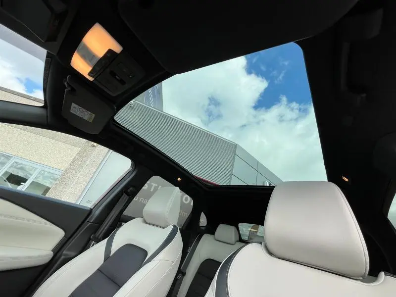 Vue intérieure du Nissan Qashqai e-POWER 2023 avec toit panoramique en verre et sièges cuir clair à surpiqûres noires.