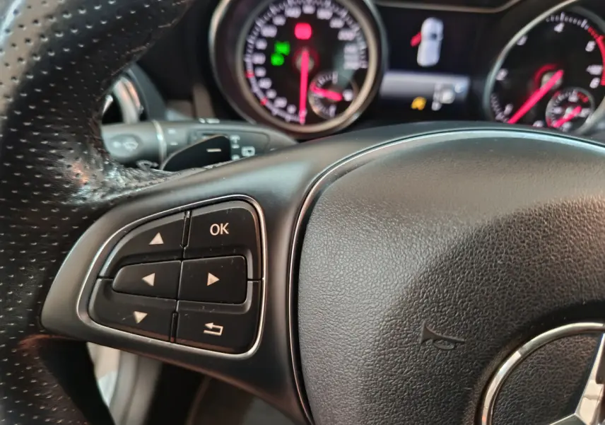 Gros plan sur le volant cuir noir de la Mercedes GLA 200 d, avec commandes multifonctions et tableau de bord lumineux en arrière-plan.