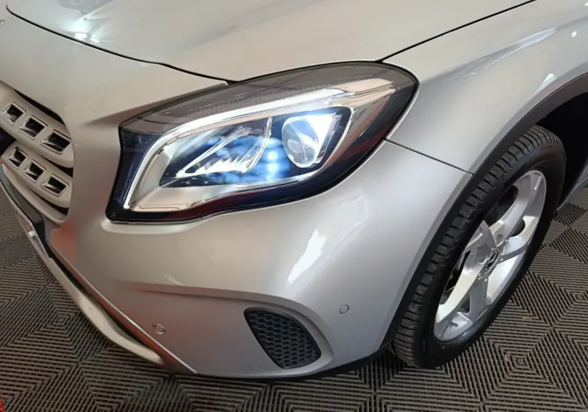 Gros plan sur l'avant droit gris clair du Mercedes GLA 200 d, mettant en valeur le phare LED allumé et la roue.