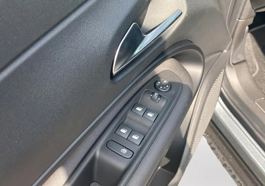 Gros plan sur la commande des vitres et rétroviseurs côté conducteur d'une Alfa Romeo Junior grise, intérieur noir.