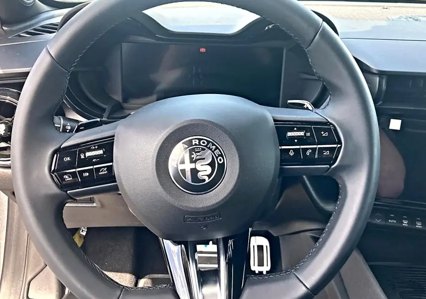 Vue rapprochée du volant noir de l'Alfa Romeo Junior 1.2 hybride, avec commandes intégrées et tableau de bord numérique.