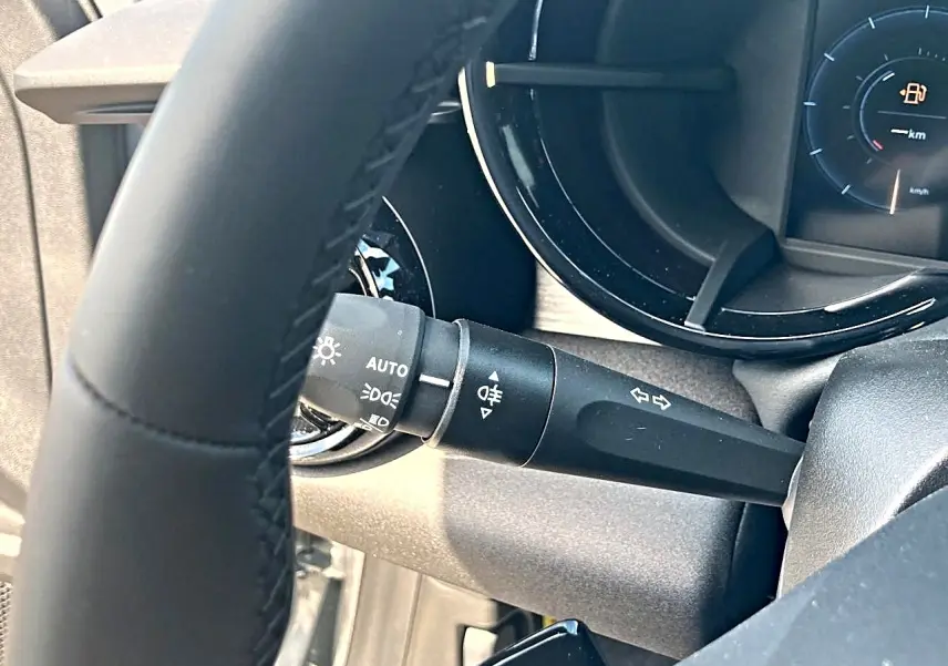 Gros plan sur le commodo d’éclairage à gauche du volant gris de l’Alfa Romeo Junior 1.2 hybride 2026.