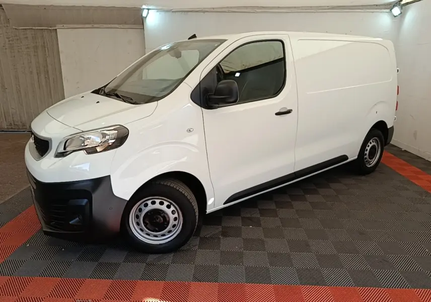 Vue 3/4 avant droit du Peugeot Expert Fourgon blanc avec pare-chocs noirs et jantes acier en intérieur fermé.