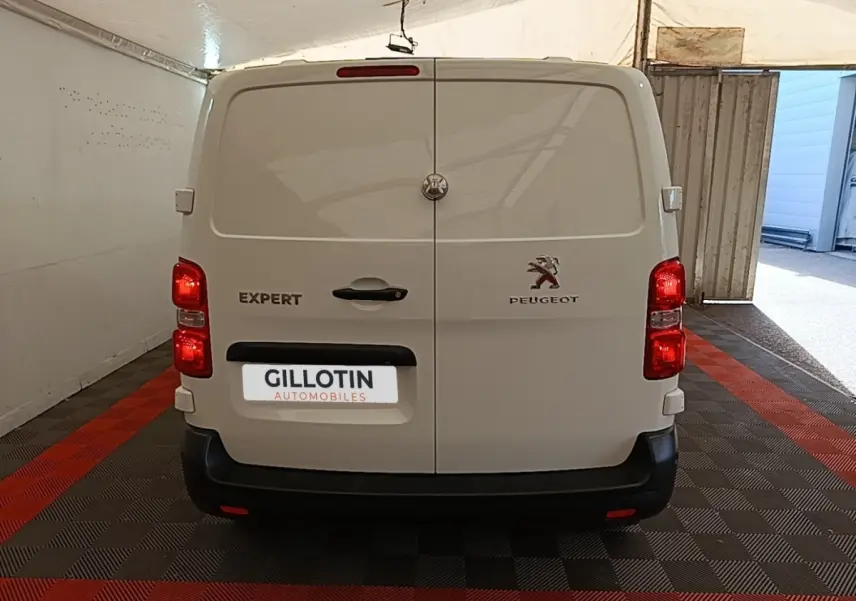 Vue arrière d’un Peugeot Expert Fourgon blanc stationné en intérieur, feux arrière allumés et porte double fermée.