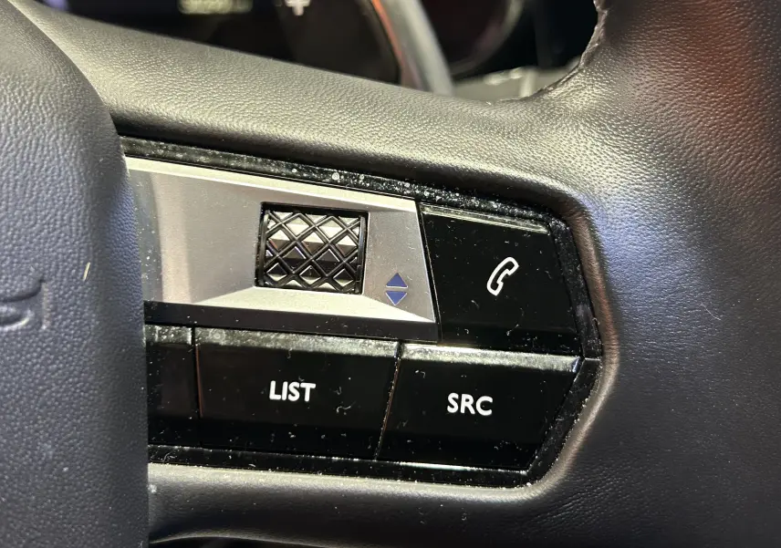 Gros plan sur les commandes noires et argentées au volant du DS7 BlueHDI 130 2024, finition cuir noir.