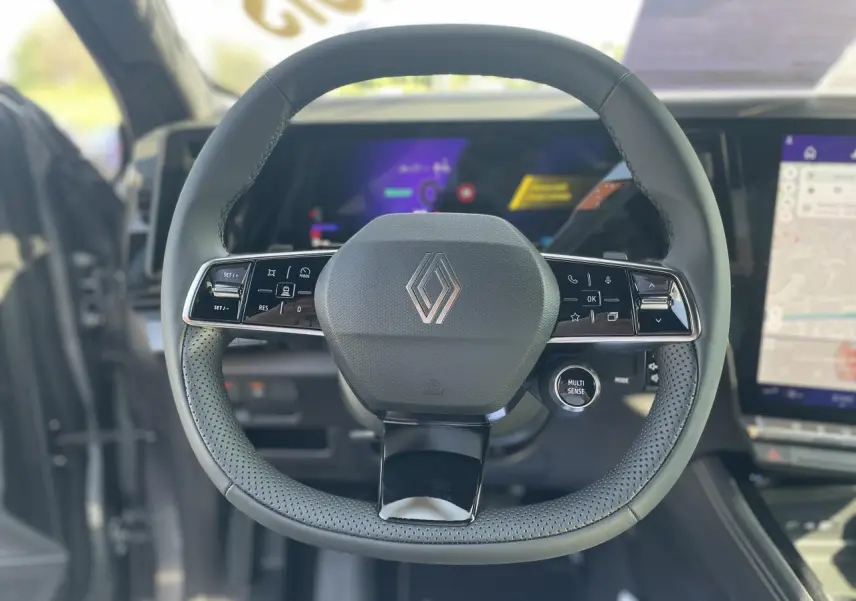 Vue rapprochée du volant noir perforé de la Renault Rafale 2025 avec commandes intégrées et logo central chromé.