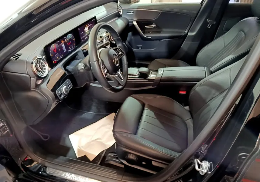 Vue intérieure côté conducteur de la Mercedes Classe A Berline noire, avec tableau de bord numérique et sièges cuir noirs.