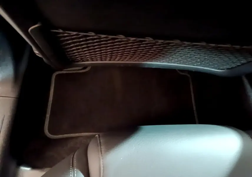 Vue intérieure du coffre arrière d'une Mercedes Classe A berline noire, montrant le tapis de sol et un filet de rangement.