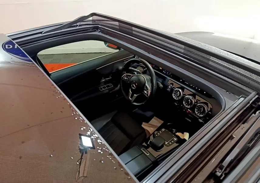 Vue intérieure par le toit ouvrant d'une Mercedes Classe A noire, mettant en valeur le volant cuir et la console centrale moderne.