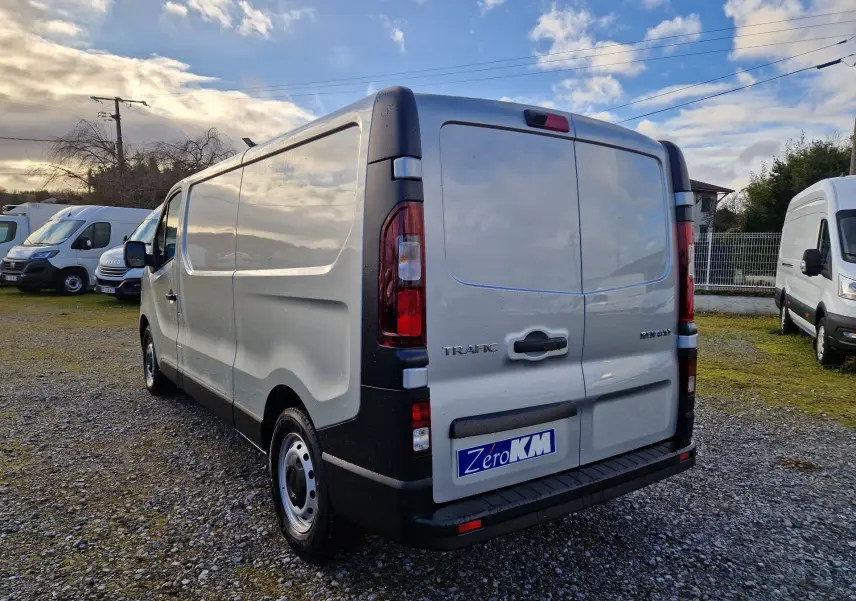 Vue 3/4 arrière droite d’un Renault Trafic Fourgon gris Highland avec portes arrière fermées sur un sol gravillonné.