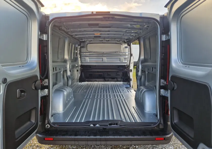 Vue arrière ouverte du Renault Trafic Fourgon gris Highland 2025, montrant l’espace de chargement vide et métallique.