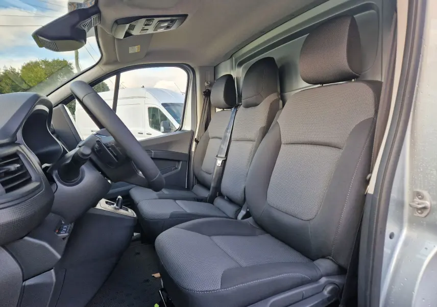 Vue intérieure côté droit du Renault Trafic Fourgon gris Highland, montrant les sièges avant et la cloison avec trappe de charge.