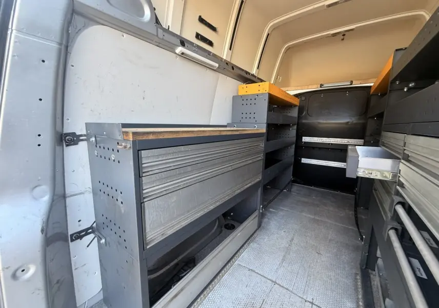 Vue intérieure arrière du Volkswagen Transporter gris clair 2022, montrant l'aménagement avec étagères et rangements métalliques.