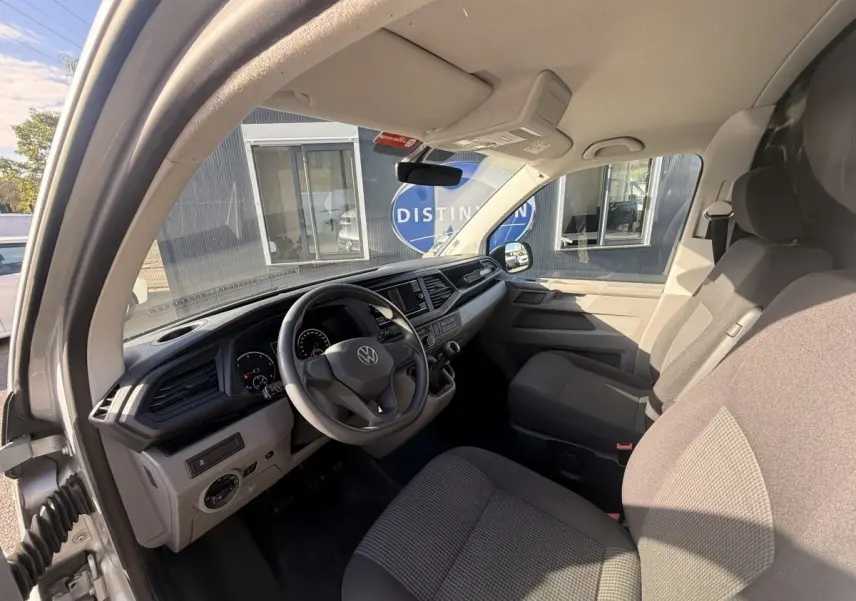 Vue intérieure côté conducteur du Volkswagen Transporter gris clair 2022, montrant le tableau de bord et les sièges avant.