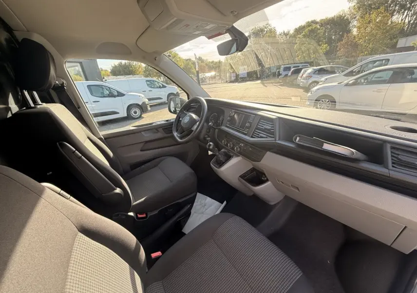 Vue intérieure côté conducteur du Volkswagen Transporter gris clair 2022, tableau de bord et sièges avant visibles.