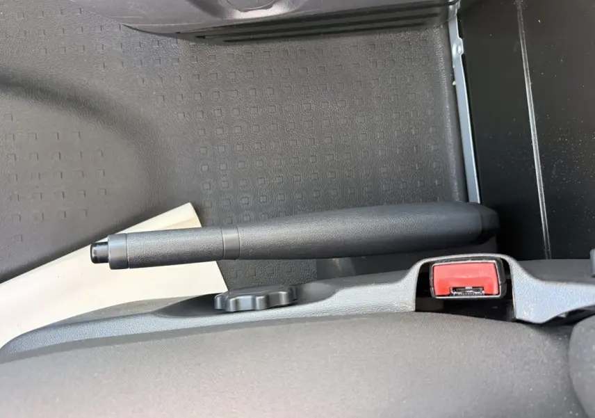 Vue rapprochée de la poignée de frein à main noire et de la ceinture de sécurité rouge dans un Volkswagen Transporter gris clair.