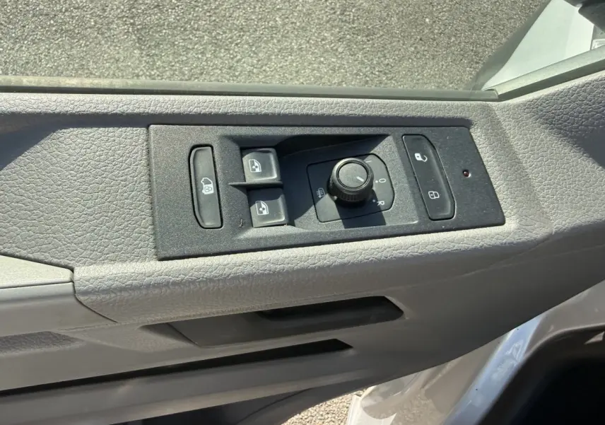 Détail des commandes de réglage des rétroviseurs et des vitres sur la porte côté conducteur d’un Volkswagen Transporter gris clair.