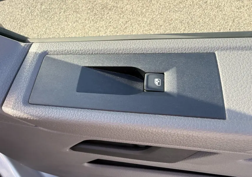Gros plan sur le bouton de commande de la vitre électrique côté conducteur d’un Volkswagen Transporter gris clair 2022.