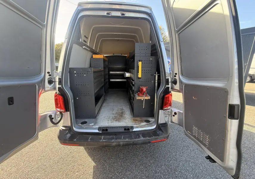 Vue arrière ouverte d’un Volkswagen Transporter gris clair 2022 avec aménagements de rangement noirs dans la zone de chargement.