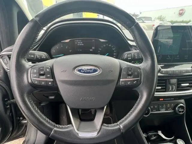 Vue centrée sur le volant en cuir noir d'une Ford Fiesta 2018, avec tableau de bord digital et écran tactile visible.