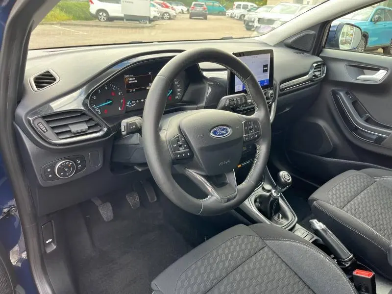 Intérieur avant gauche du Ford Puma bleu 2023, volant multifonction, boîte manuelle et sièges tissu noir Kasbah.