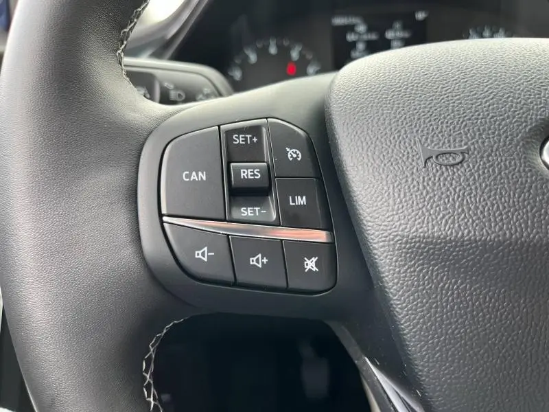 Gros plan sur les commandes du volant multifonction côté gauche du Ford Puma bleu 2023, avec boutons de régulateur et volume.