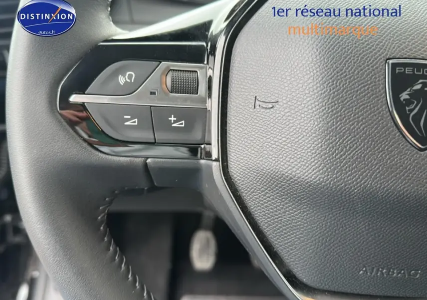 Gros plan sur le volant noir de la Peugeot 208 1.2 100 style avec commandes audio intégrées à gauche.