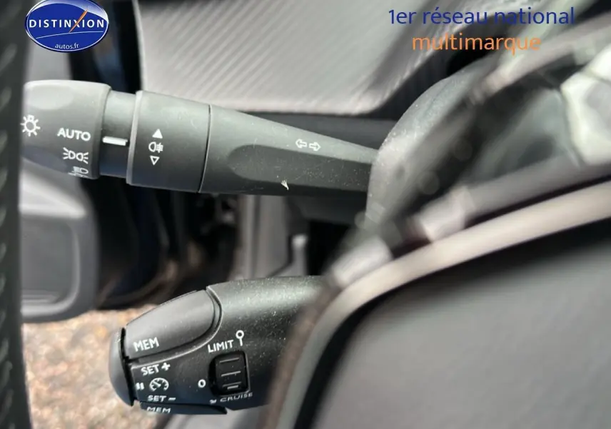Gros plan sur les commandes au volant de la Peugeot 208 noire, mettant en valeur les fonctions de régulateur et feux.
