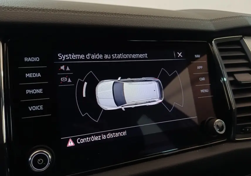 Écran tactile intérieur montrant le système d'aide au stationnement avec vue aérienne du Skoda Kodiaq blanc.