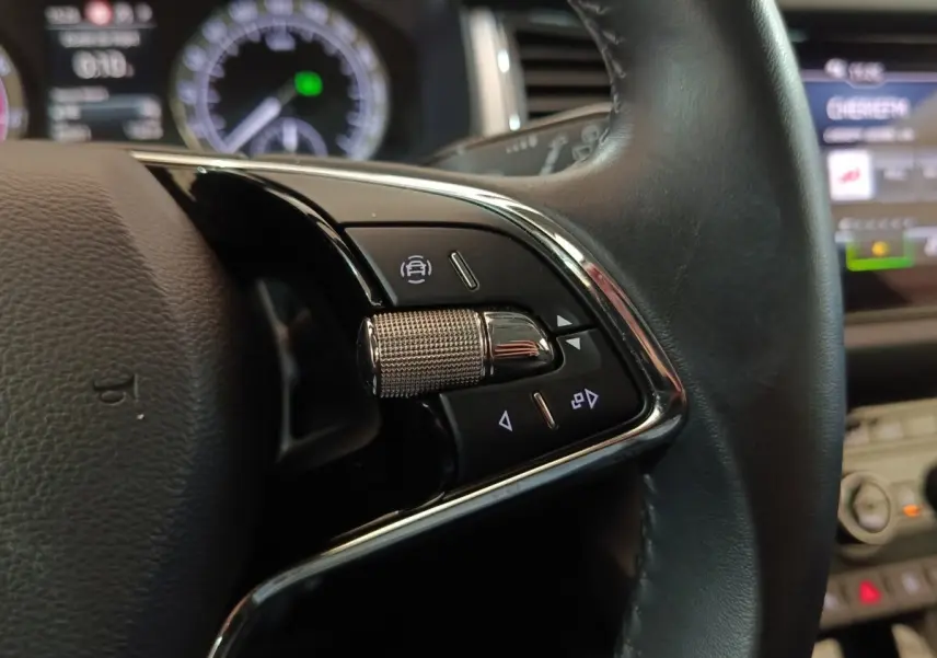Gros plan sur les commandes multifonctions côté gauche du volant cuir noir d’un Skoda Kodiaq blanc, affichage digital en arrière-plan.