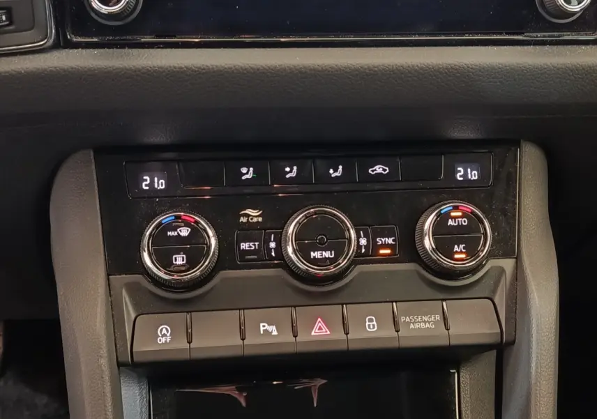 Vue rapprochée du tableau de bord noir du Skoda Kodiaq blanc, montrant les commandes de climatisation digitale et les boutons fonctionnels.