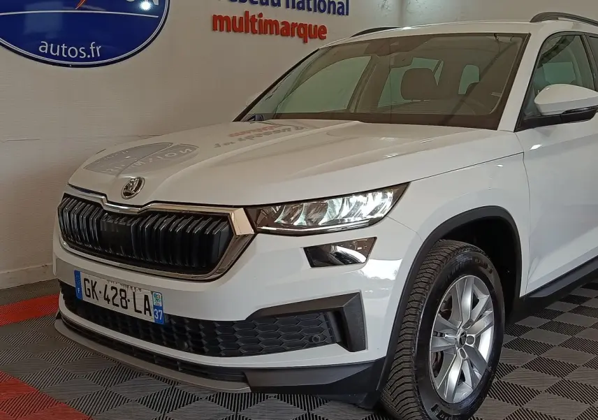 Vue 3/4 avant d'un Skoda Kodiaq blanc 2022 avec calandre noire et phares LED dans un showroom.