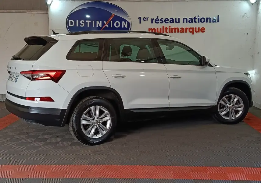 Vue de profil côté gauche d'un Skoda Kodiaq blanc 7 places, avec jantes alliage et toit noir en arrière-plan intérieur showroom.