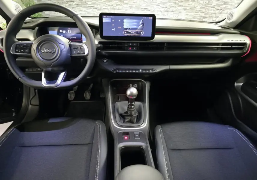 Vue intérieure avant du Jeep Avenger 2025 noir, volant multifonction, écran tactile central et levier de vitesses manuel.