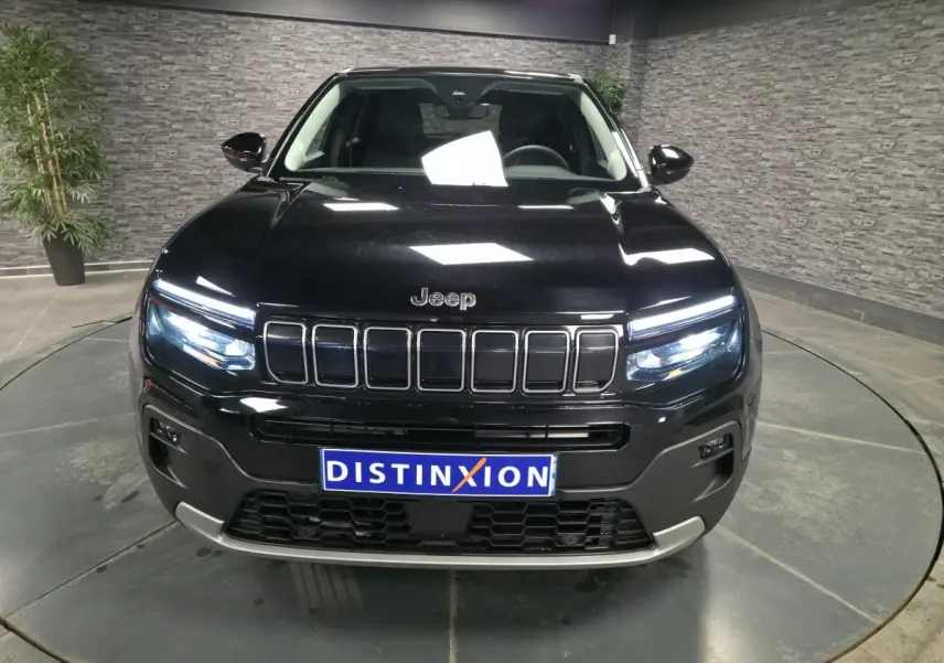 Vue frontale du Jeep Avenger noir 2025 avec calandre gloss black et phares LED allumés dans un showroom.