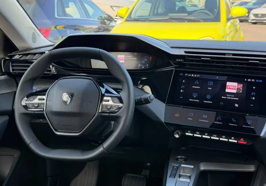 Vue intérieure centrée sur le volant multifonction et l’écran tactile de la Peugeot 308 hybride 2025.
