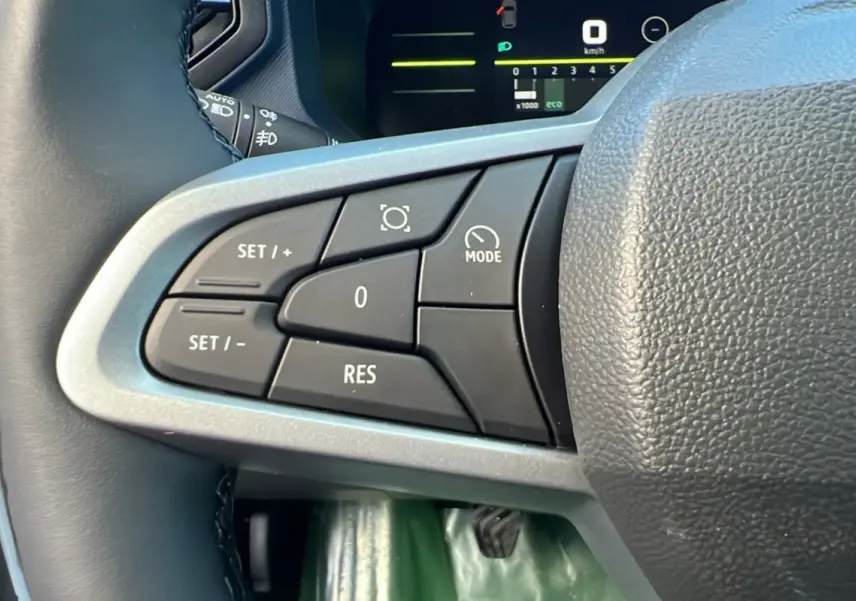 Gros plan sur les commandes au volant côté gauche du Dacia Duster blanc glacier 2025, affichage digital en arrière-plan.