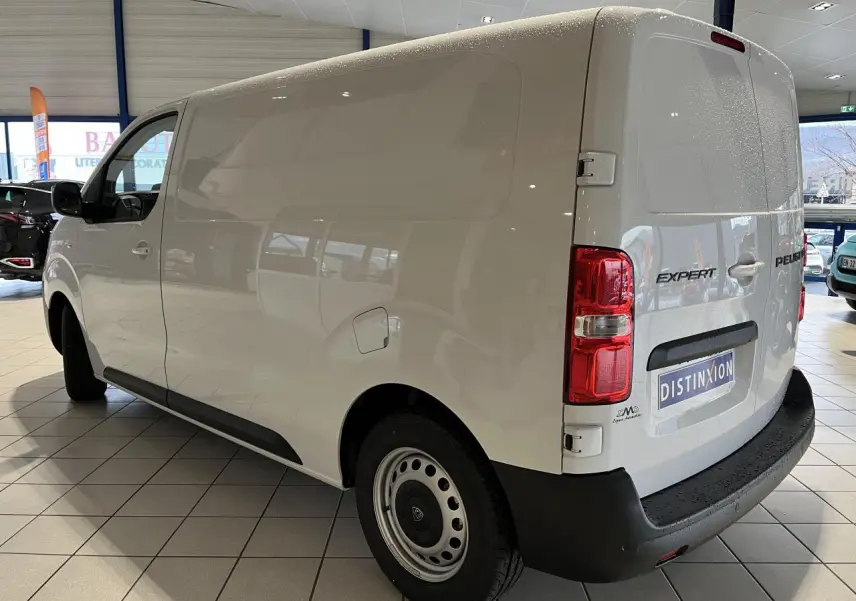 Vue 3/4 arrière droite du Peugeot Expert Fourgon blanc avec roues tôles grises et pare-chocs noirs en intérieur showroom.