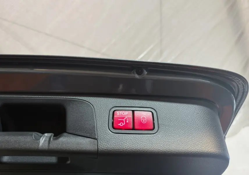 Boutons rouges d'ouverture et fermeture électrique du coffre sur le bord intérieur du hayon d'un Mercedes GLC gris foncé.