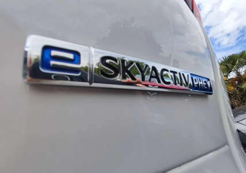 Gros plan sur l'emblème e-SKYACTIV PHEV chromé sur la carrosserie blanche métallisée d'un Mazda CX-60 2024.