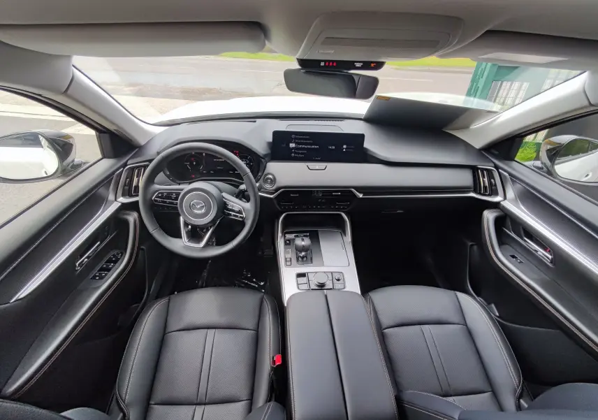 Vue intérieure avant du Mazda CX-60 blanc métal 2024, tableau de bord moderne avec écran central et sièges cuir noir.