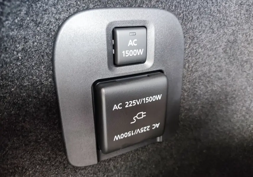 Prise électrique 1500W en gros plan dans le coffre du Mazda CX-60 hybride rechargeable blanc métal 2024.