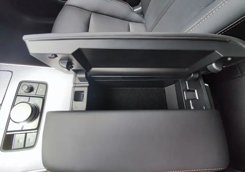 Vue rapprochée de l'accoudoir central ouvert en cuir noir avec surpiqûres jaunes dans le Mazda CX-60 2024.