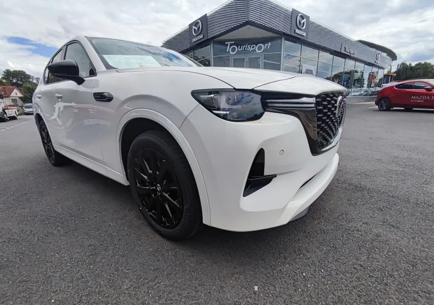 Vue 3/4 avant gauche du Mazda CX-60 blanc métal avec jantes noires, devant un concessionnaire Mazda Tourisport.