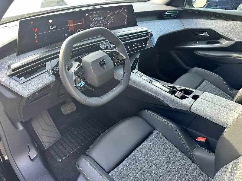 Intérieur avant du Peugeot 3008 2025, vue côté conducteur, avec tableau de bord numérique et sellerie tissu gris et cuir noir.